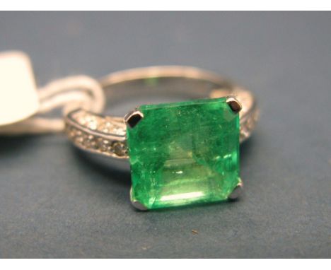 A Modern Emerald and Diamond Set Ring, the (9mm) central square cut emerald, four claw set high between diamond set shoulders