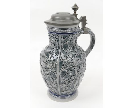 Decorative German glazed pitcher, having a hinged pewter cover, the body relief moulded throughout with a reveller seated on 