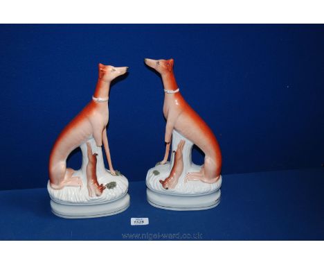 A pair of Staffordshire Greyhounds in seated position with tree trunk support and hare at foot, on waisted oval bases, sadly 