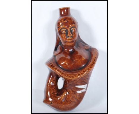 A mid 19th century treacle glaze gin flask in the form of a mermaid. Circa 1840, with waisted top above the head.Measures 21c