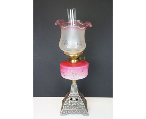 Late Victorian / early 20th Century oil lamp having a cast metal base with pink glass reservoir with floral scrolled details 