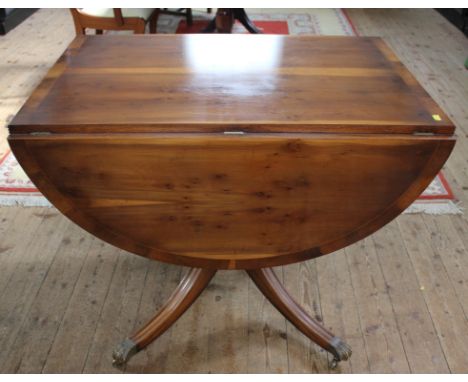 A Regency-style yew wood and cross banded drop leaf table with fluted rim, urn shaped central column on a quadruped base with