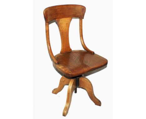 A 1920s light oak swivel office chair with shaped top rail, urn shaped support, dished seat on a quadruped base 