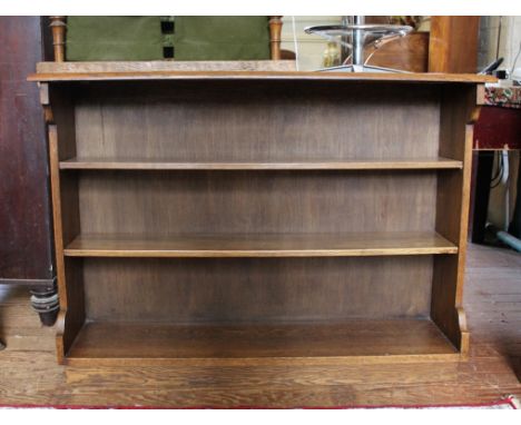 An early 20th century light oak free-standing bookcase with shaped top, adjustable shelving on a platform base, 113cm wide
