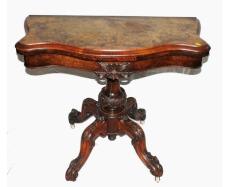 A Victorian mahogany and walnut card table with shaped top, applied carving to the frieze, raised on a profusely carved balus