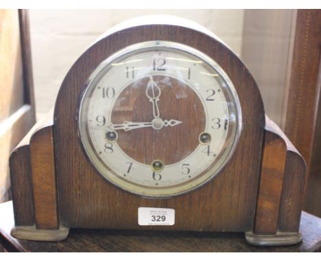 An Art Deco oak-cased dome shaped mantle clock with Arabic numerals on a stylized base