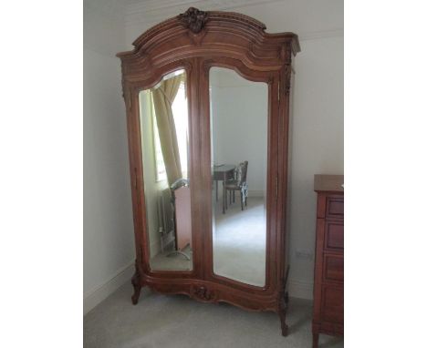 A 19th century French walnut armoire having an arched, carved crest, over a pair of bevelled mirrored doors, enclosing a shel