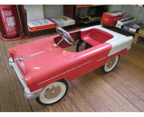 A pink and cream child's pedal car in the style of a Chevrolet car