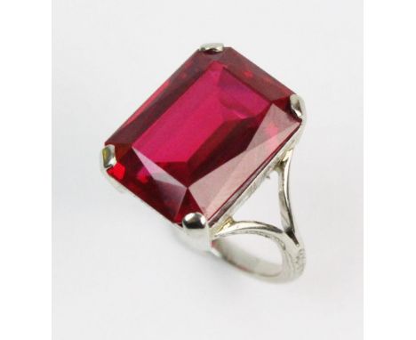 An Art Deco style stone set ring, the central mixed cut untested red stone measuring 15mm x 12mm, claw set in white metal to 