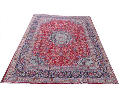 A Persian Kashan wool carpet, worked with a central blue medallion against a floral red ground, 378cm x 293cm (worn) For cond