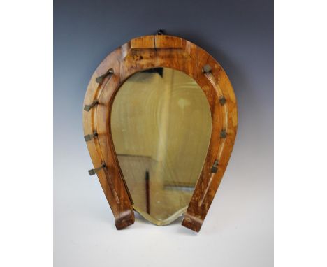 A mirrored horse whip rack, early 20th century, the walnut rack of horseshoe form, set with four over-size horseshoe nails on