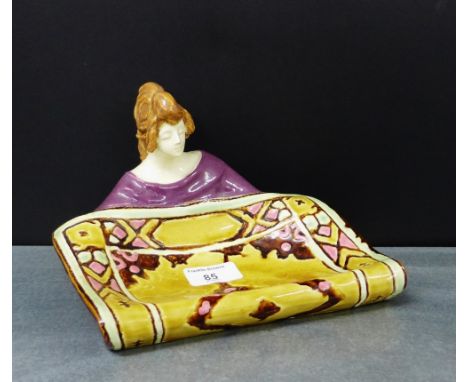 An Art pottery dish modelled as a female unrolling a carpet, apparently unmarked, 15 x 20cm 