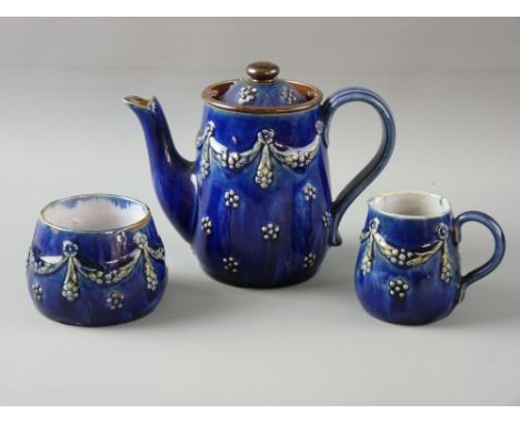 A ROYAL DOULTON STONEWARE THREE PIECE TEA SERVICE with raised swag and floral decoration on a cobalt ground, impressed factor