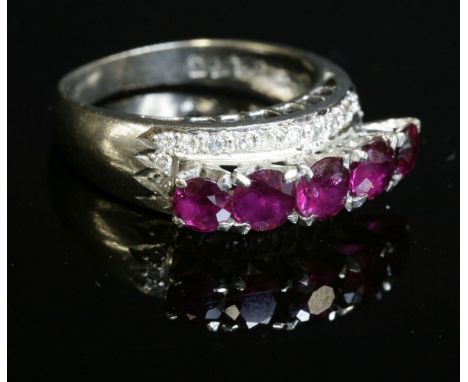A ruby and diamond ring, c.1970, with a row of graduated, circular mixed cut rubies, four claw set in a row to tall wigwam co