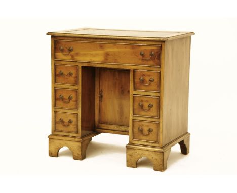 A George I design yew wood kneehole desk, the lined top above central cupboard, encompassed by seven drawers on bracket feet,