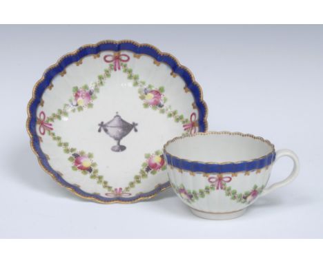 A Worcester reeded French shaped teacup and saucer, painted with deep purple classical urns,  within puce ribbon tied foliate
