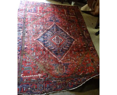 A Heriz Carpet with a lozenge shape centre panel, surrounded by stylised leaves on a red field and bordered.  9'4" (285cms) x