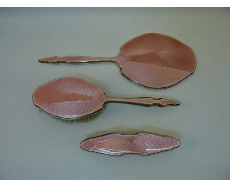 A three piece silver mounted and pink enamel Dressing Table Set comprising hand mirror, clothes brush and hair brush, Birming