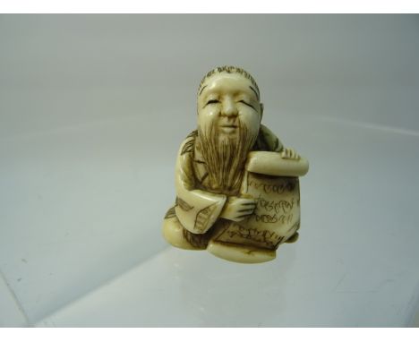 A late 19th Century Japanese carved ivory Netsuke in the form of a seated sage holding a scroll.  