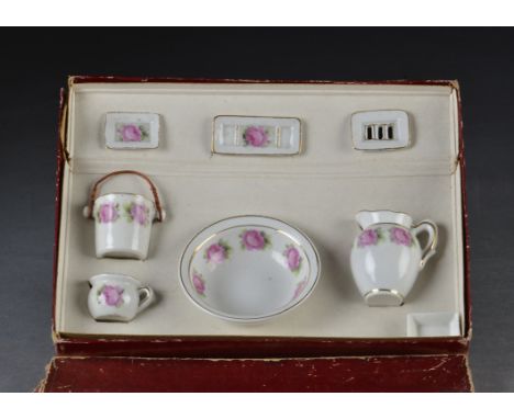 A doll’s boxed wash set, porcelain water jug, basin, chamber pot, slop bucket, soap dish and two other dishes, transfer decor