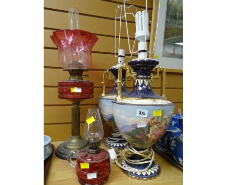 An antique oil lamp with cranberry glass reservoir and shade together with a pair of pottery table lamps and a smaller oil la