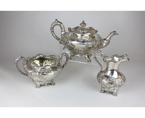 A George IV Victorian silver matched three piece tea set of teapot, circular shape with embossed scrolls and flowers, maker J