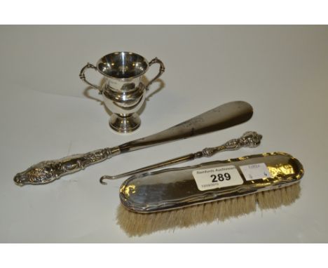 A silver hafted shoe horn;  a silver hafted button hook;  a silver backed clothes brush;  a silver two handled trophy 