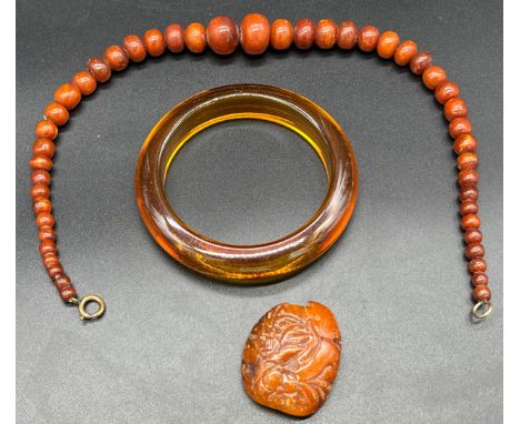 Three items of amber, Includes graduated bead necklace, carved ingot/ pendant and bangle. 