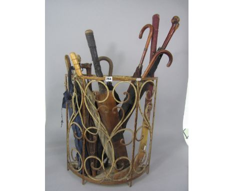 Early 20th century wrought iron bow shaped stick stand containing a collection of sticks and umbrellas to include a parasol w