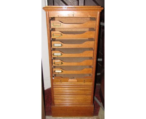 An early 20th century medium to light oak floor standing filing cabinet enclosed by a rise and fall tambour door with index t