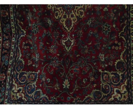 A heavy Persian wool carpet with central medallion upon a red ground, with scrolling floral detail, within alternating blue a