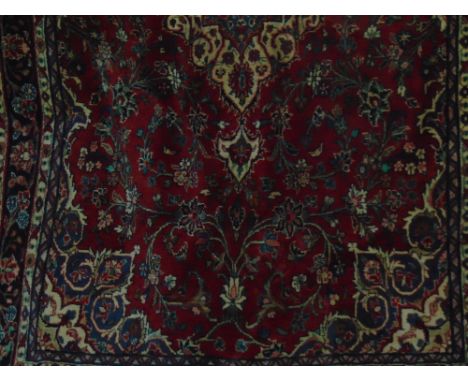 A heavy Persian wool carpet with central medallion upon a red ground, with scrolling floral detail, within alternating blue a