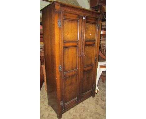 An old English style oak wardrobe enclosed by a pair of full length triple moulded panelled doors with exposed hinges and sli