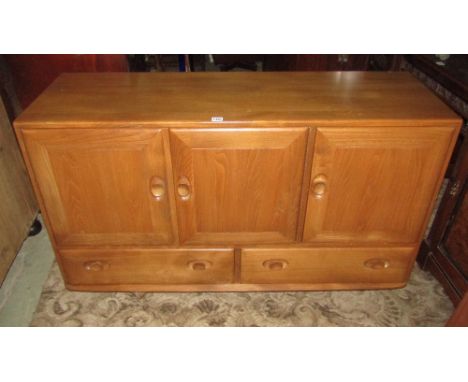 An Ercol light elm low sideboard enclosed by three rectangular doors over two drawers with dished handles