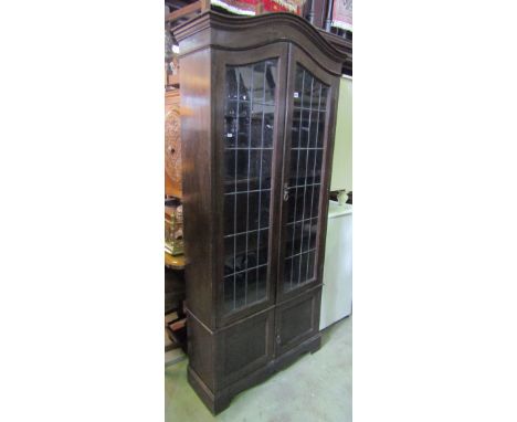 An Edwardian/1920s oak bookcase/side cabinet, freestanding and enclosed by two pairs of panelled doors, the upper glazed lead