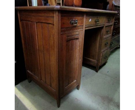 A late Victorian oak kneehole twin pedestal writing desk fitted with an arrangement of six drawers and cupboard with tramline