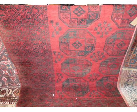 An Afghan wool carpet, the black geometric detail upon a mid red ground, within alternating geometric borders, 300 x 260cm 