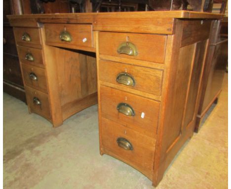 A medium to light oak kneehole twin pedestal desk fitted with an arrangement of nine drawers with brass cup handles, 4ft wide