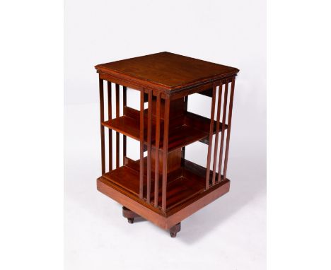 AN EDWARDIAN WALNUT ROTATING BOOKCASE with cast iron brackets to the stand and on ceramic casters, the top 50cm square, the b