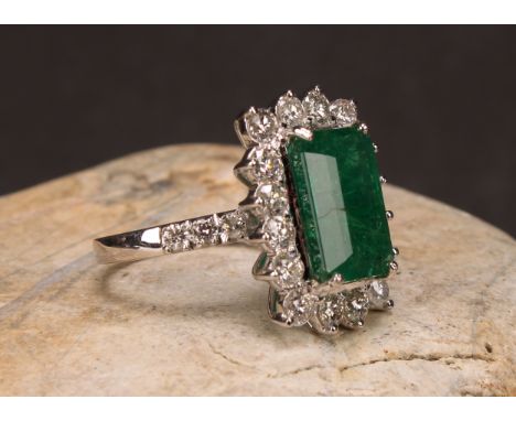 An 18ct white gold emerald and diamond cluster ring, step-cut emerald, 6.01ct, round brilliant cut diamonds 1.70ct, Cert no. 