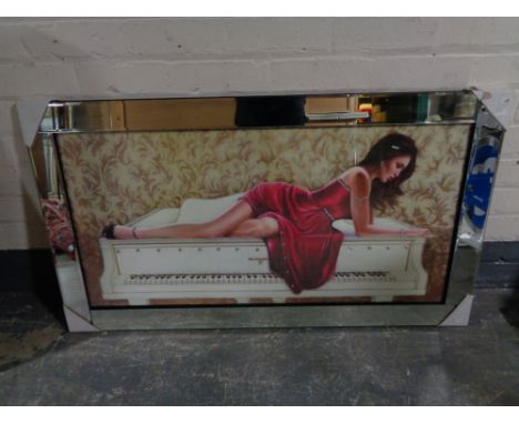 A contemporary framed print of a lady in red dress reclining on a grand piano, with glitter decoration, in mirrored frame 