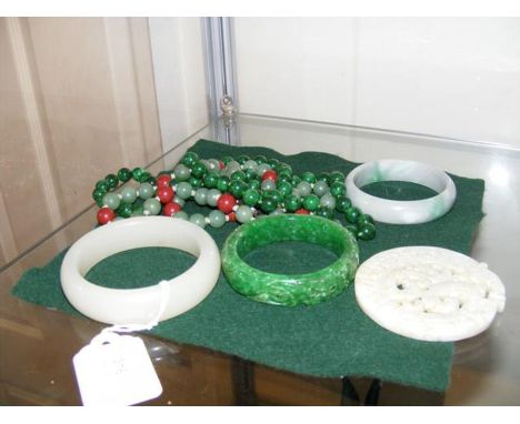 A 8.5cm jade bangle, together with two others, two necklaces and carved disc