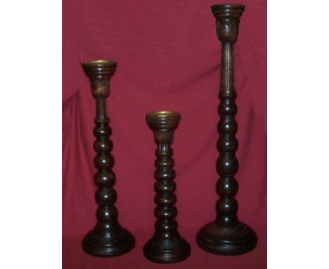 An oak Church Candlestick on knulled column and circular base, 2' 6" (76cms) high, and two smaller matching Candlesticks.
