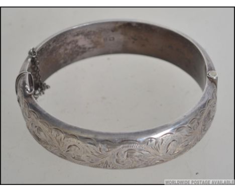 A silver rococo chased hallmarked bangle by SPS&CO bearing Birmingham hallmarks for 1963. Complete with safety chain. Total w