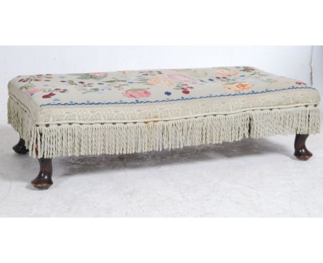A 1930's tapestry upholstered mahogany footstool raised on stub cabriole legs with pad feet having tapestry long upholstered 