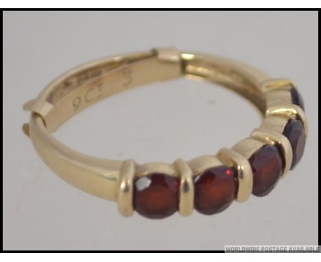 A 9ct gold hallmarked ladies dress ring being channel set with 5 ruby garnet stones. The ring with adjustable sizer also mark