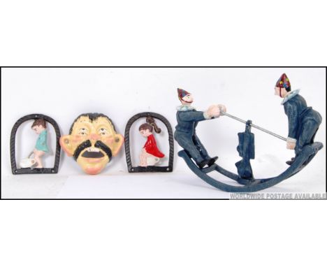 Three cast iron items. One of two Jesters riding a Seesaw, two wall plaque, one of a boy going to the toilet, the other a gir