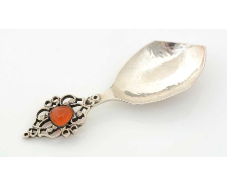 A George V silver caddy spoon, with a hammered and pointed bowl and a pierced scrollwork terminal, cabochon set with an orang