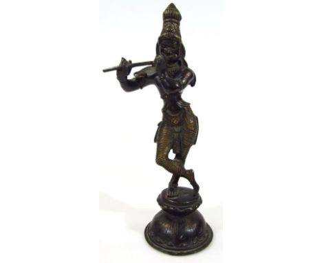 A 19thC bronze Indian figure of Krishna dressed in finery, in standing pose playing flute on a shaped domed concave base, unm