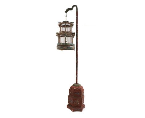 A Chinese circular wooden birdcage on stand, of red lacquered wood with chinoserie decoration, hanging on a painted pole with